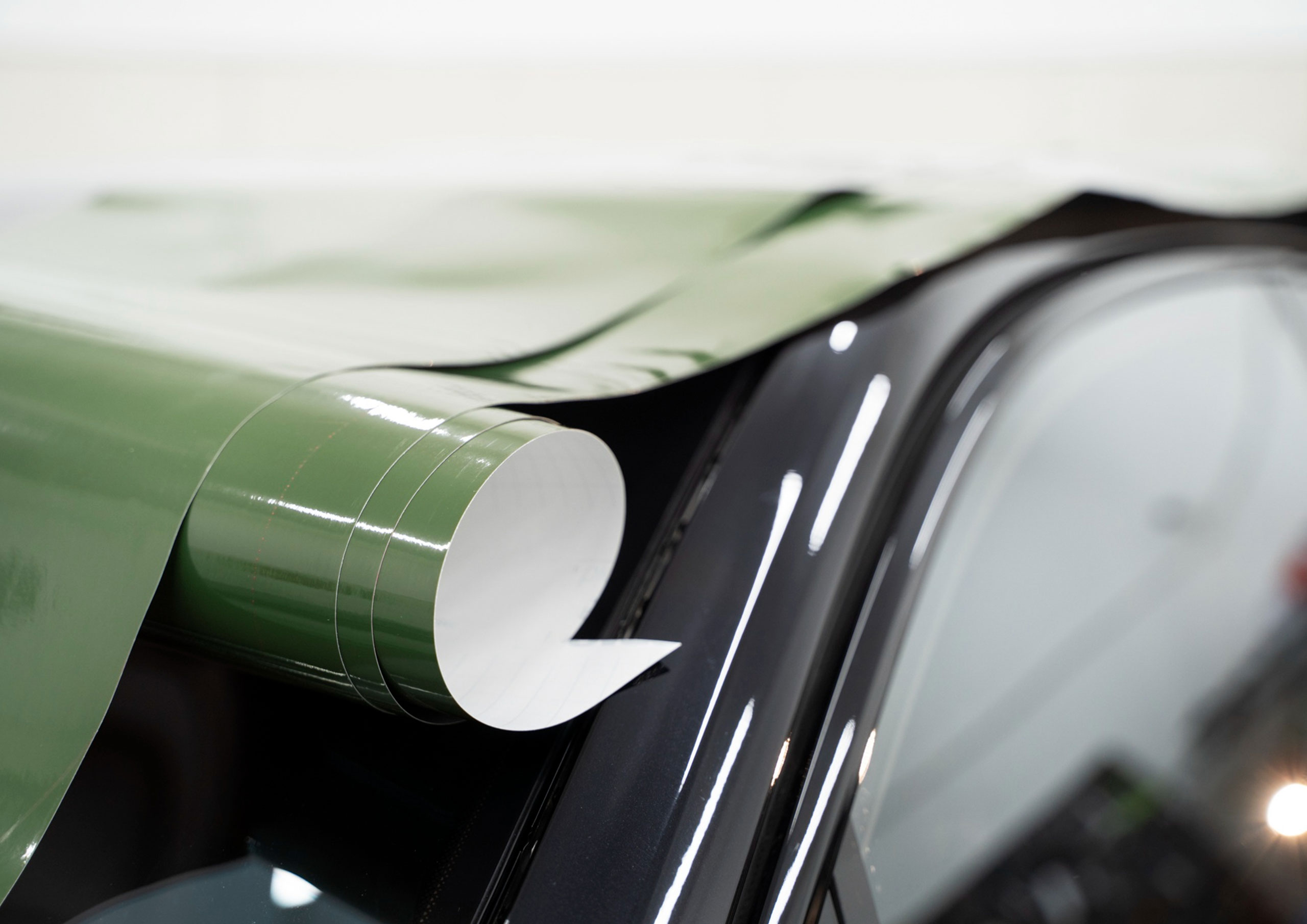 Detalle de vinilo adhesivo verde brillante siendo aplicado sobre la carrocería de un vehículo por Gabella Artes Gráficas en Norte, Sevilla, ideal para rotulación profesional.